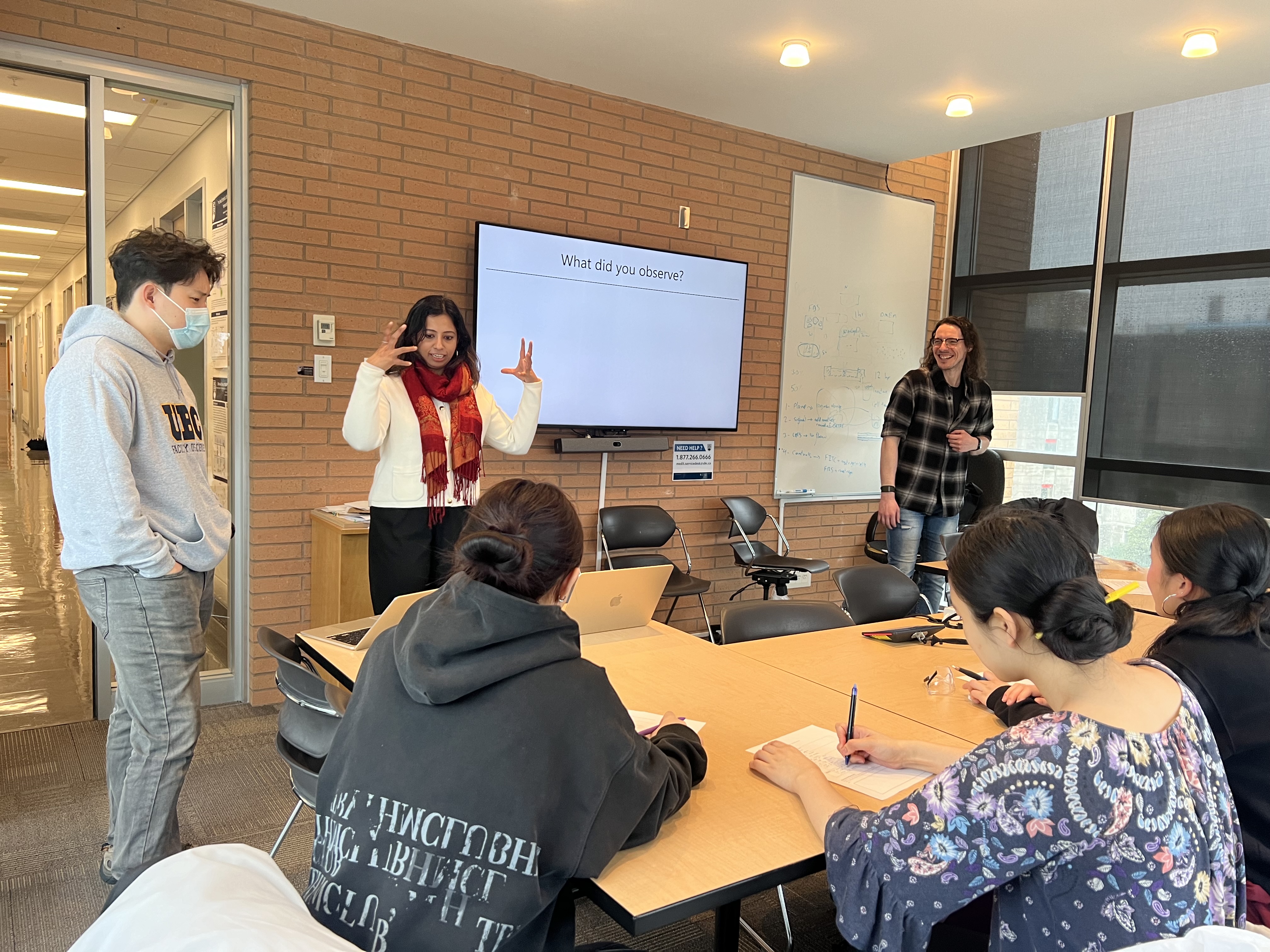 Three people lecture at the front of a classroom