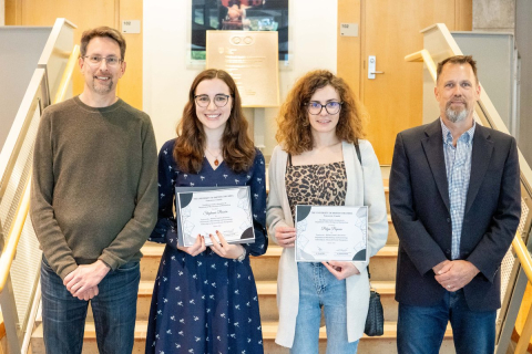 Dr. Michael Murphy, Stephanie Besoiu, Petya Popova, and Dr. Martin Hirst are standing in a row smiling with the two women in the middle holding their awards.